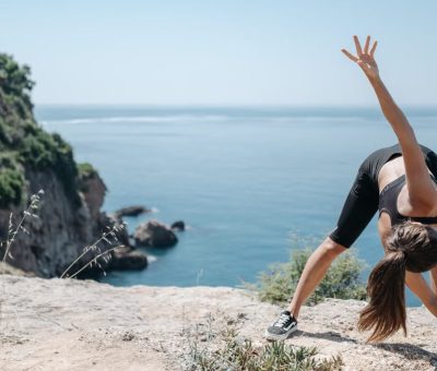 A woman in activewear stretching on a cliff with a stunning ocean view, embracing a fitness lifestyle.