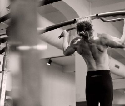 Focused on a man doing pull-ups in a gym, showcasing strength and fitness.